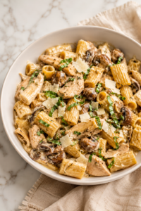 Creamy chicken Marsala mushroom pasta served in a white bowl with rigatoni, tender chicken, mushrooms, parmesan cheese, and a rich Marsala cream sauce on a marble countertop.