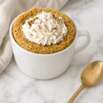 Easy pumpkin mug cake topped with whipped cream and pumpkin pie spice in a white mug on a marble countertop.