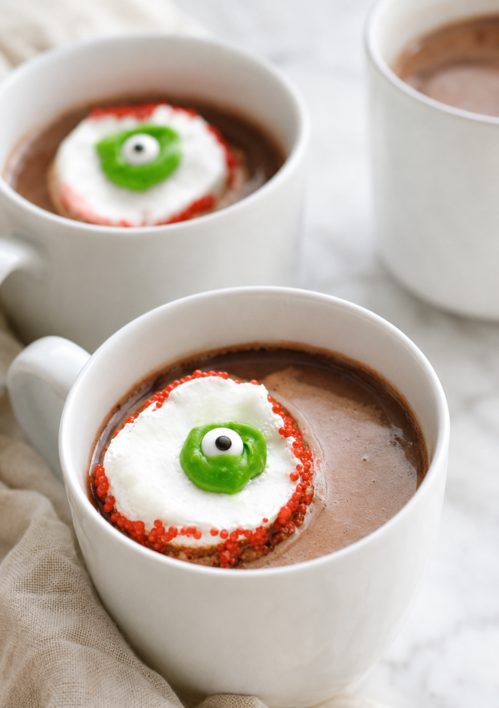 Homemade marshmallow eyeball floating in a white mug of creamy hot chocolate for Halloween.