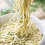 Creamy fresh herb fettuccine Alfredo with parsley and basil, soft-focus close-up of noodles being lifted from a white bowl