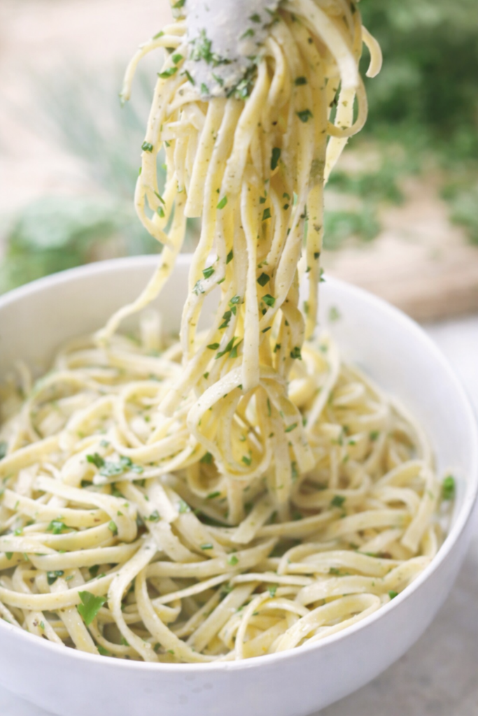 Creamy fresh herb fettuccine Alfredo with parsley and basil, soft-focus close-up of noodles being lifted from a white bowl