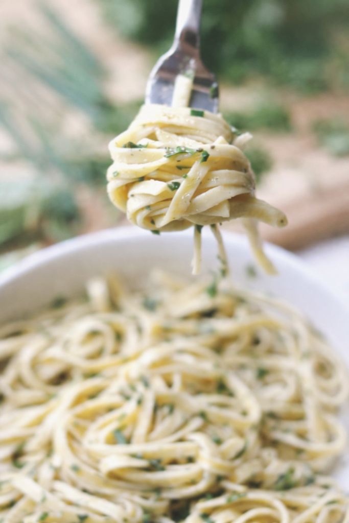 Fork lifting creamy fresh herb fettuccine Alfredo with parsley and chives, soft focus close-up over a bowl of pasta