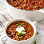 Mild Boilermaker-style turkey chili with Italian turkey sausage, beans, tomatoes, sour cream, and green onions in a white enamel Dutch oven