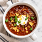 Bowl of mild turkey chili with Italian turkey sausage, beans, sour cream, green onions, and crushed corn chips