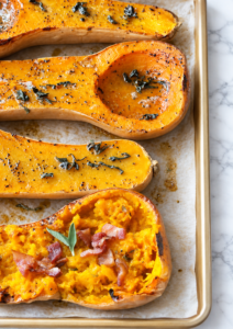 Maple bacon butternut squash halves roasting with fresh sage on a parchment-lined sheet pan