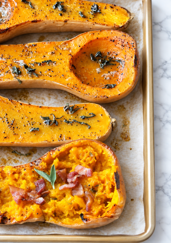 Maple bacon butternut squash halves roasting with fresh sage on a parchment-lined sheet pan