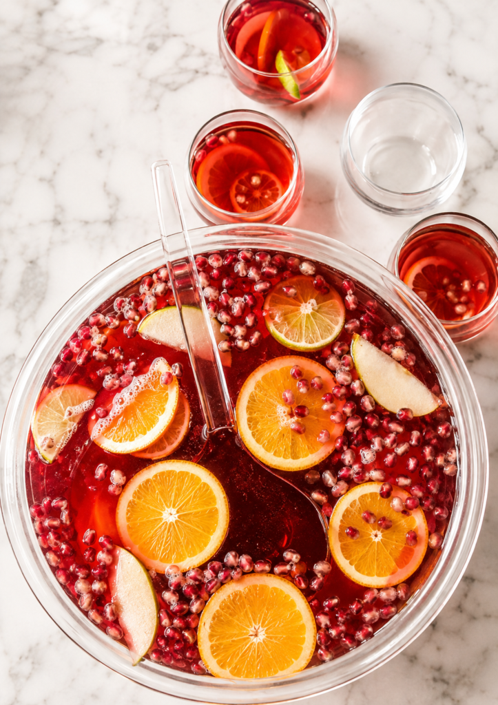 Easy holiday punch with Prosecco, cranberry juice, fresh orange slices, lime, pear, and pomegranate seeds in a glass punch bowl.