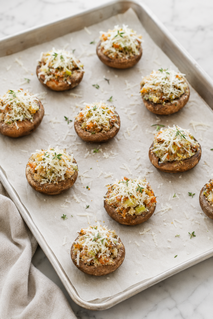 Stuffing stuffed mushrooms topped with Parmesan and fresh thyme on a parchment-lined baking sheet before baking.