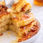 Bite of cornmeal bacon pancake on a fork with melted honey butter dripping down.