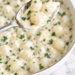 Creamed pearl onions in a garlic herb cream sauce served in a white dish with a silver spoon
