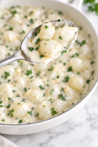 Creamed pearl onions in a garlic herb cream sauce served in a white dish with a silver spoon