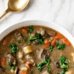 Overhead view of creamy pot roast stew with tender beef, potatoes, carrots and mushrooms beside a gold spoon.