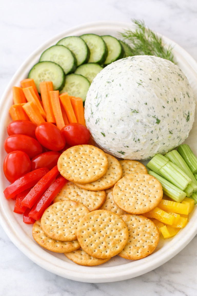 Homemade Boursin cheese ball on a white platter with crackers, cucumber slices, tomatoes, carrots, celery, and bell peppers on a marble counter