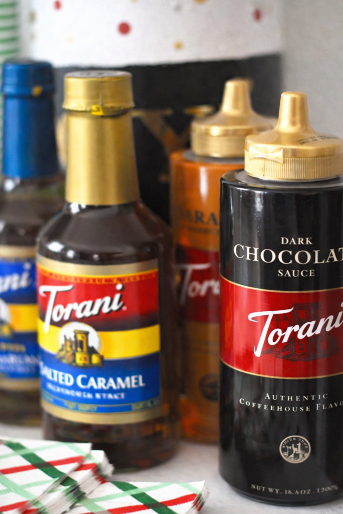 Flavored syrup bottles for a hot chocolate bar, including chocolate and caramel toppings styled for holiday entertaining.