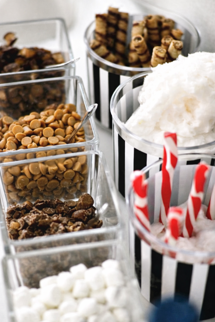 Assorted hot chocolate bar toppings including marshmallows, chocolate chips, caramel bits, wafer cookies, and peppermint sticks.