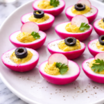 Close-up of pickled beet deviled eggs with pink edges on a white platter over a marble counter