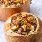 Bacon cheeseburger soup served in a bread bowl with a copper pot of soup in the background
