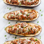 Stuffed eggplant parmesan boats filled with hearty Italian meat sauce and topped with freshly grated Parmesan cheese on a light marble countertop.