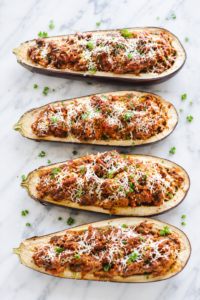 Stuffed eggplant parmesan boats filled with hearty Italian meat sauce and topped with freshly grated Parmesan cheese on a light marble countertop.