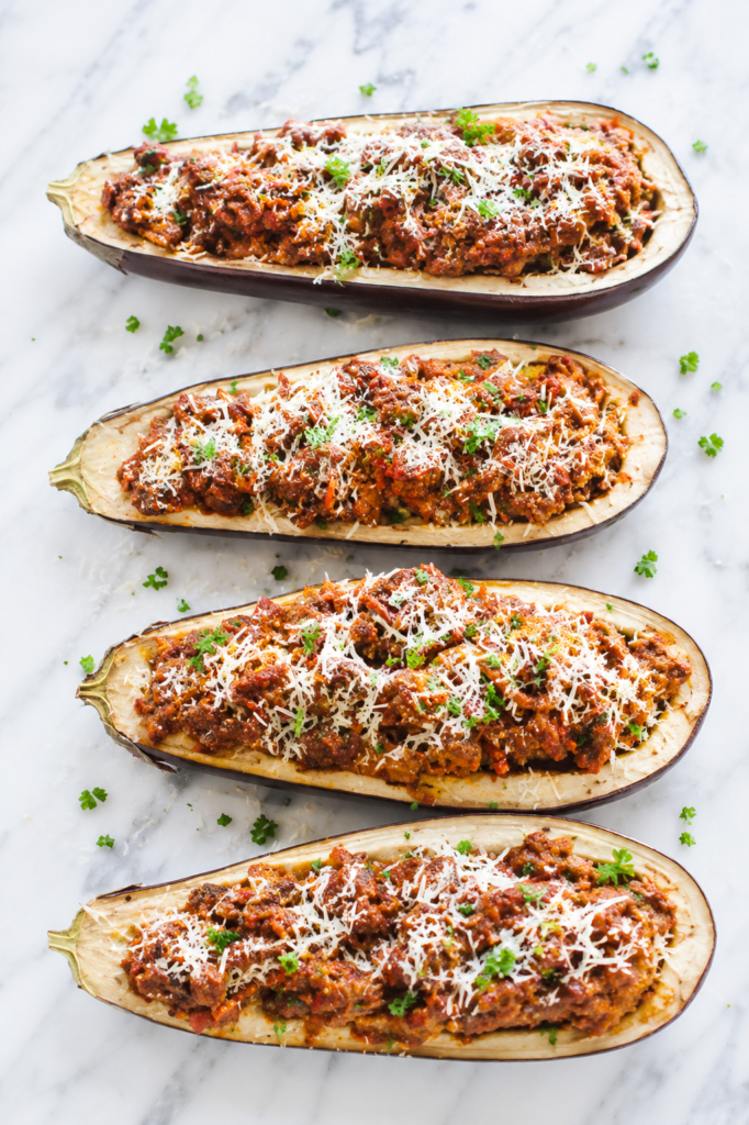 Stuffed eggplant parmesan boats filled with hearty Italian meat sauce and topped with freshly grated Parmesan cheese on a light marble countertop.
