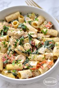 Creamy Dijon chicken pasta with sun-dried tomatoes and spinach in a white bowl