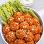 Baked buffalo chicken ball bites topped with blue cheese and celery in white bowl