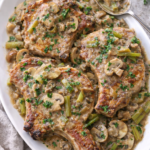Pork chops served on a white platter with creamy mushroom and onion gravy spooned over the top