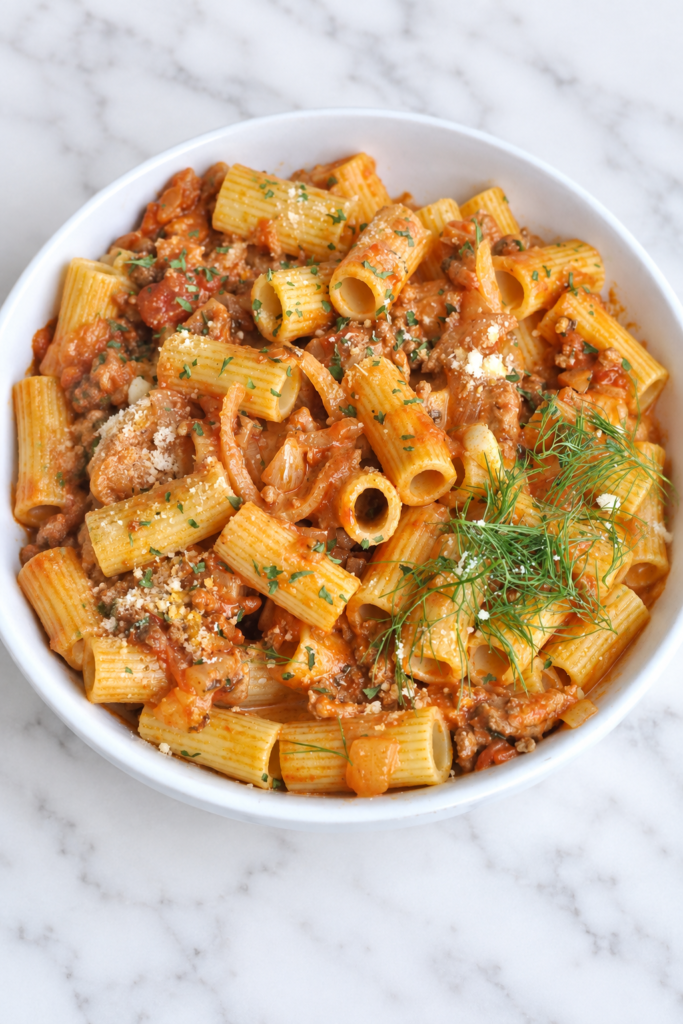 Creamy Italian sausage rigatoni with tender fennel, onions, and Pecorino Romano in a white bowl.