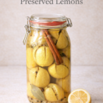 Jar of homemade preserved lemons with cinnamon stick and bay leaf on a neutral background Pinterest graphic