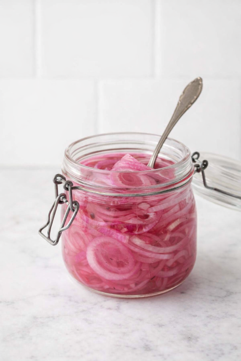 Quick pickled red onions in a glass jar on a white marble countertop with a white tile background.