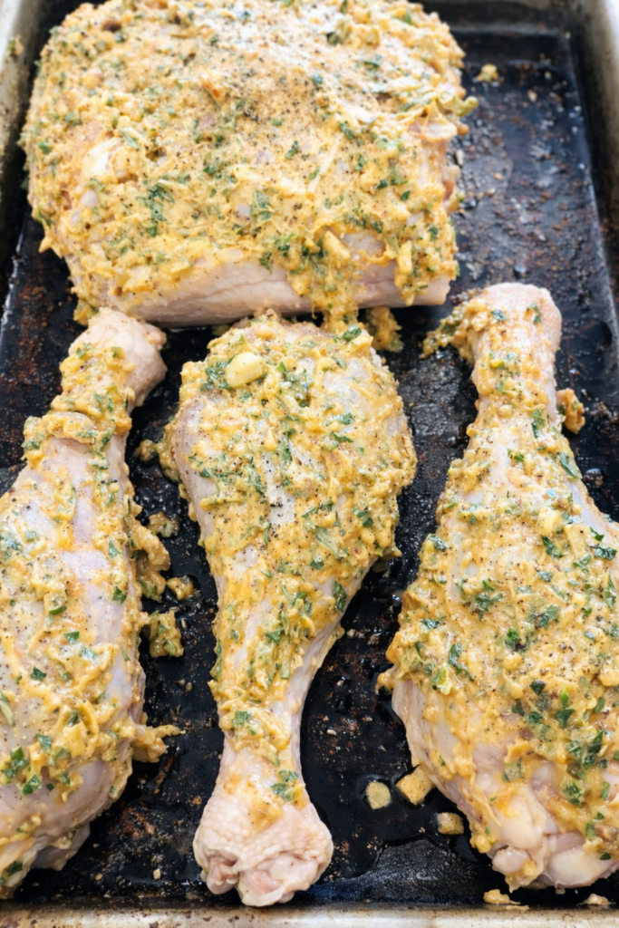 Chicken and poultry pieces coated in homemade herb compound butter on a baking sheet, ready for roasting.
