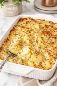 Creamy cheesy scalloped potatoes baked until golden brown in a white rectangular baking dish with a silver serving spoon.