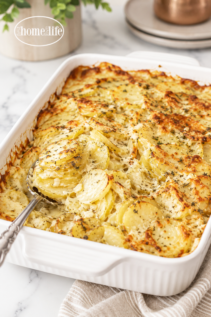Creamy cheesy scalloped potatoes baked until golden brown in a white rectangular baking dish with a silver serving spoon.