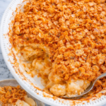 cheesy cornflake potato casserole with creamy hashbrowns and crispy topping in white baking dish on marble counter with serving spoon