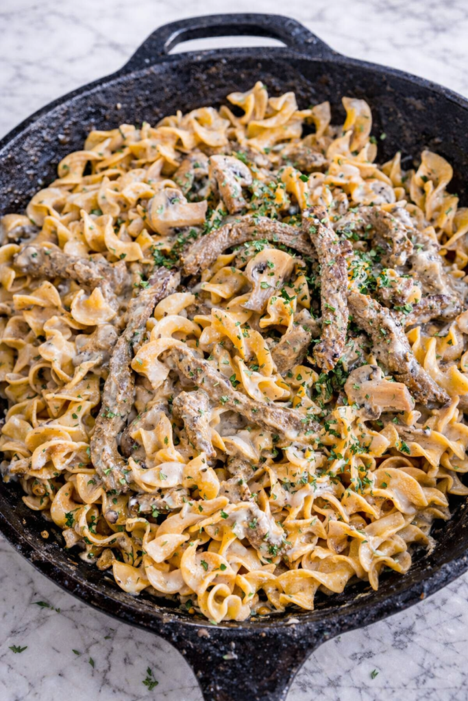 Creamy blue cheese beef stroganoff with egg noodles and mushrooms in a cast iron skillet on a marble counter