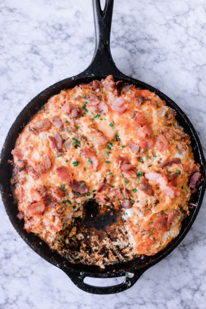 Breakfast sausage, bacon, and egg biscuit casserole baked in a cast iron skillet on a white marble countertop