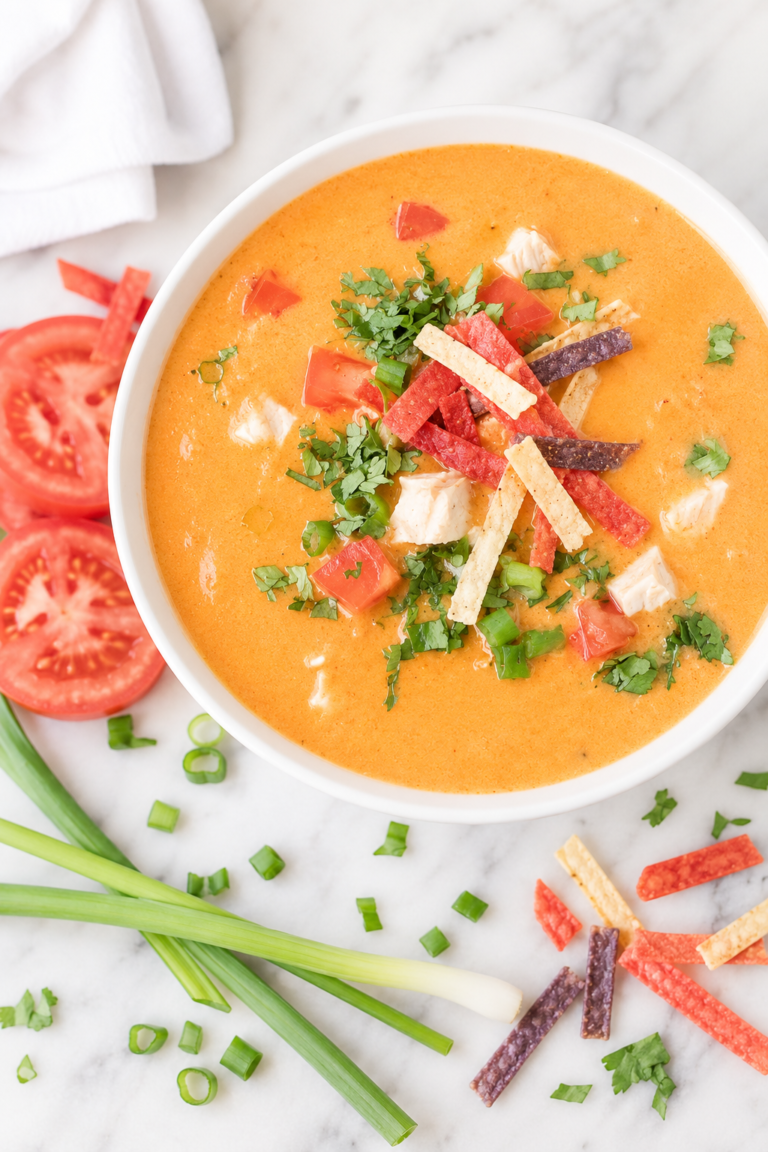 Creamy Chili's copycat chicken enchilada soup served in a white bowl on a marble countertop with tortilla strips, tomatoes, cilantro, and green onions.