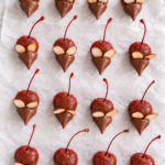Chocolate covered cherry mice with red sugar sprinkles, almond ears, Hershey’s Kiss faces, and cherry-stem tails on white parchment.