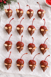 Chocolate covered cherry mice with red sugar sprinkles, almond ears, Hershey’s Kiss faces, and cherry-stem tails on white parchment.