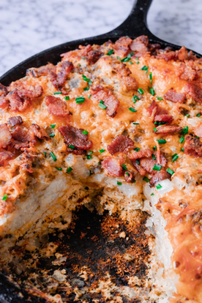 Close up of breakfast biscuit casserole with bacon and melted cheddar cheese baked in a cast iron skillet on a marble countertop