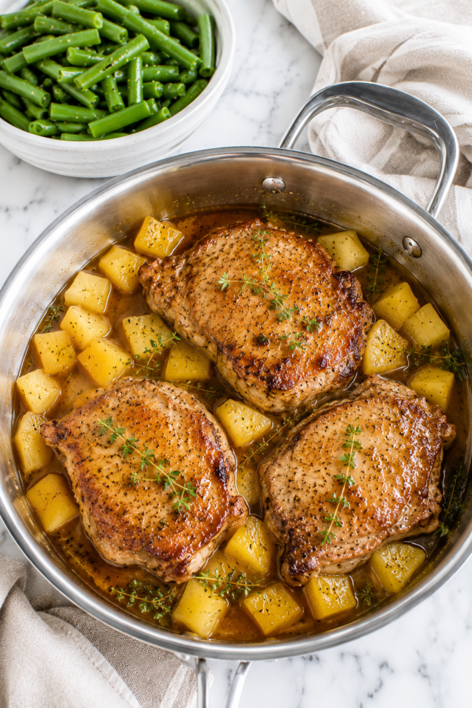 Easy pineapple pork chops cooked in a one pan skillet with fresh pineapple chunks, thyme, and a sweet savory pineapple glaze served with green beans.