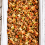 White casserole dish filled with semi-homemade chicken sausage and apple stuffing with golden bread cubes, chicken apple sausage, apples, celery, carrots, and fresh herbs.