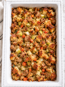 White casserole dish filled with semi-homemade chicken sausage and apple stuffing with golden bread cubes, chicken apple sausage, apples, celery, carrots, and fresh herbs.