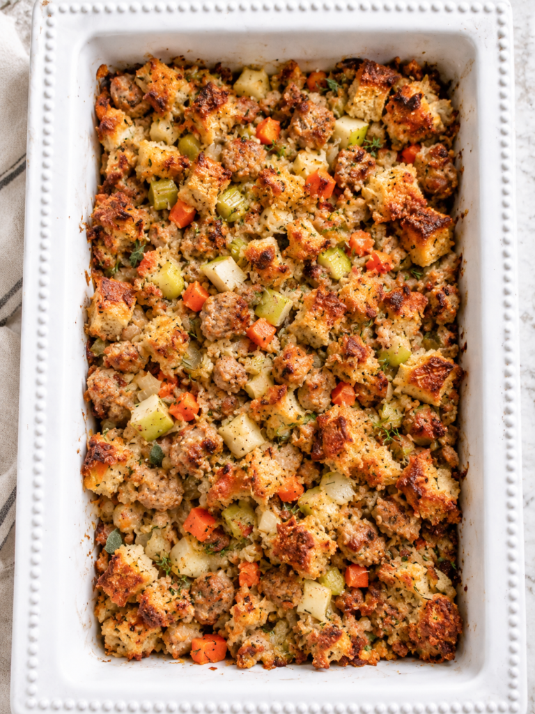 White casserole dish filled with semi-homemade chicken sausage and apple stuffing with golden bread cubes, chicken apple sausage, apples, celery, carrots, and fresh herbs.