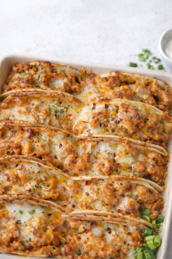 Baked chicken bacon ranch tacos with melted cheese in a white baking dish, oven baked until crispy and golden.
