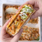 Baked chicken bacon ranch taco topped with shredded lettuce and ranch dressing, held by hand over a marble countertop.