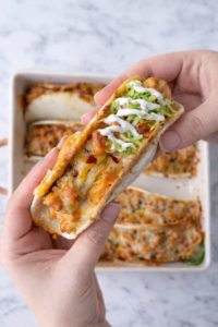 Baked chicken bacon ranch taco topped with shredded lettuce and ranch dressing, held by hand over a marble countertop.