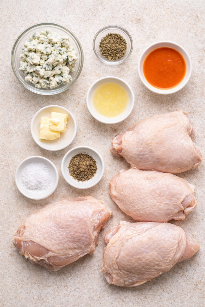 Flat lay of ingredients for blue cheese stuffed chicken breasts with buffalo wing sauce on a light surface