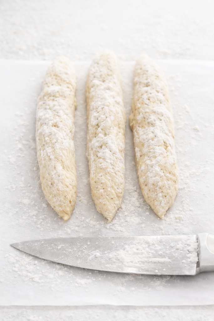 Three floured dough ropes prepared for braiding poppy seed bread on a light work surface