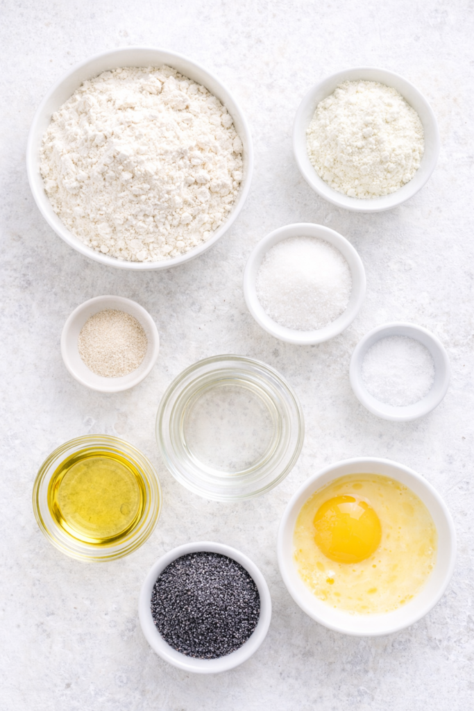 Flat lay of ingredients for braided poppy seed bread including flour, yeast, poppy seeds, oil, sugar, milk, and egg
